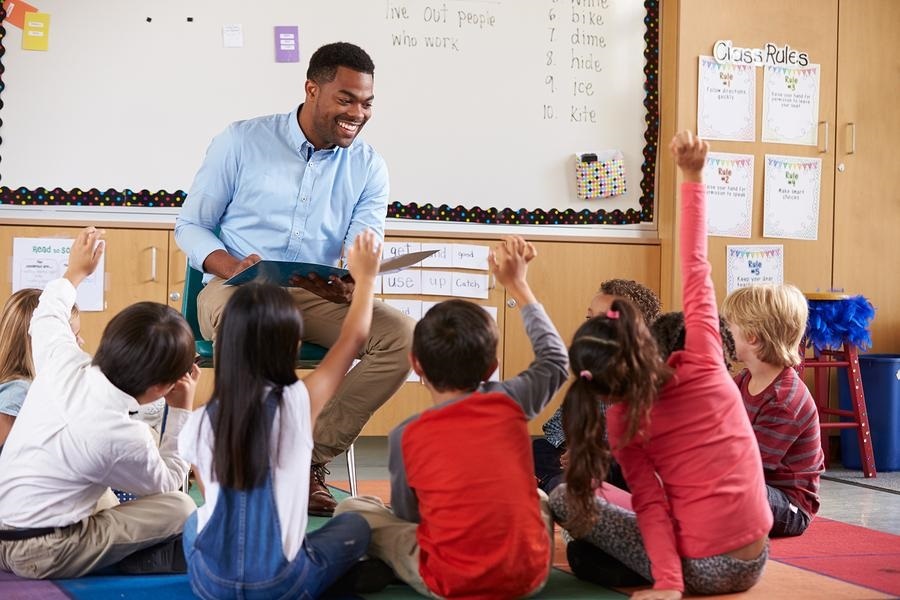 children seated on floor in class with teacher on stool