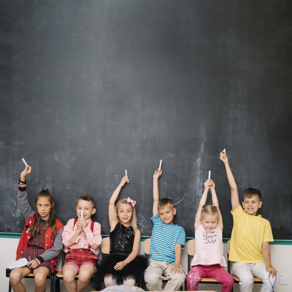 Young pupils with chalk in front of a black board