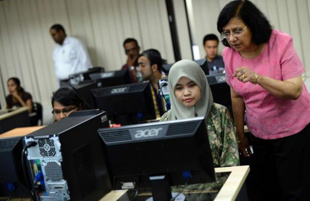 Muslim secondary school girl using a computer as a teacher watches.