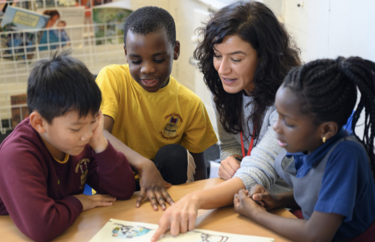 Teacher reading a book to a multi-ethnic group of schoolchildren.