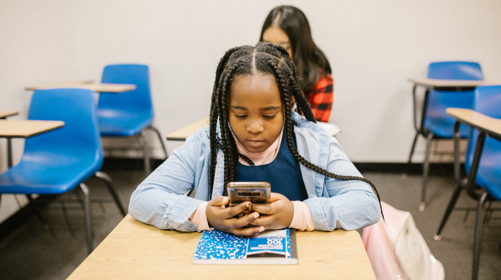 Black secondary school girl using mobile phone at her desk.