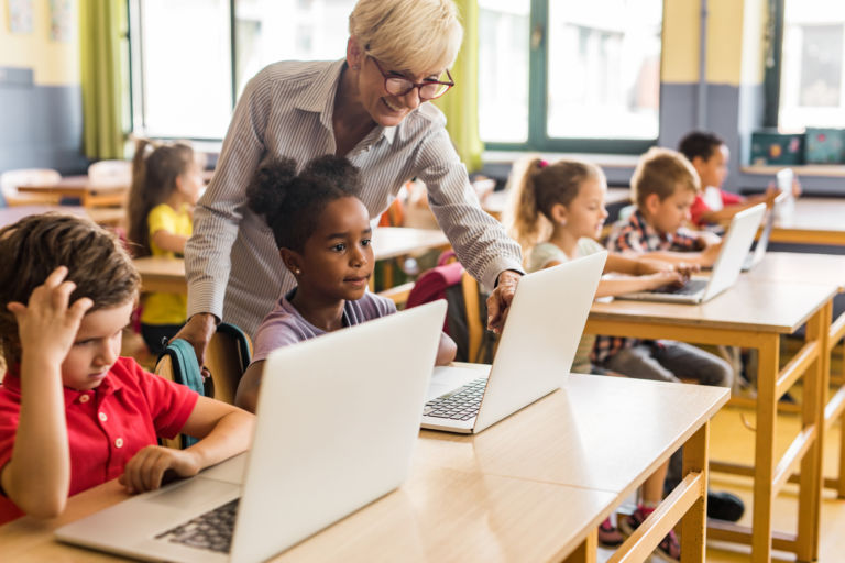Elementary school teacher helping children with laptops
