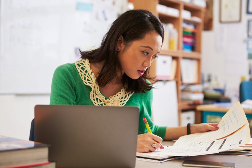 Teacher reading documents and planning a budget at her classroom desk.