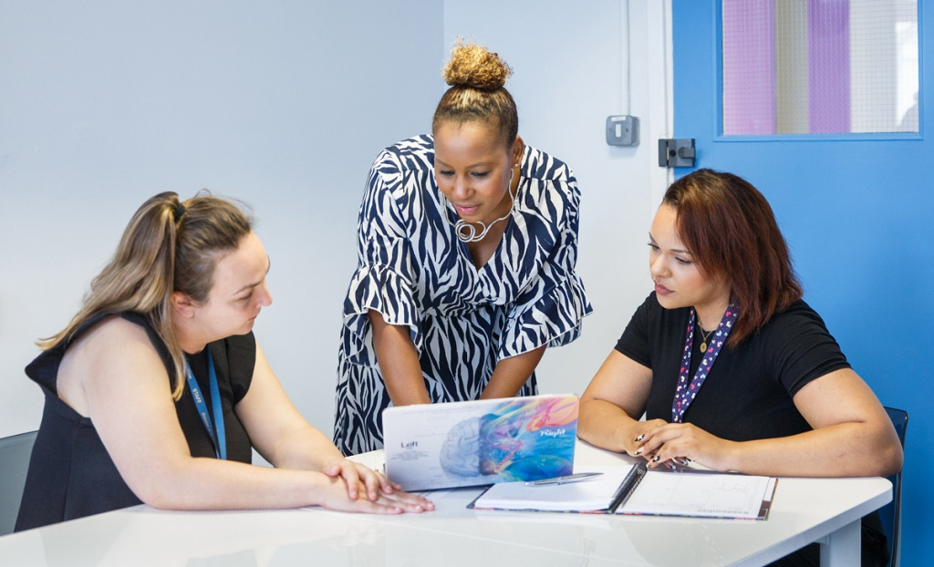 Three female teachers discuss strategy in a staff room.