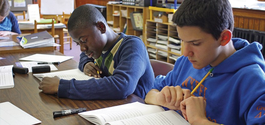 Two secondary school boys reading textbooks in a classroom.