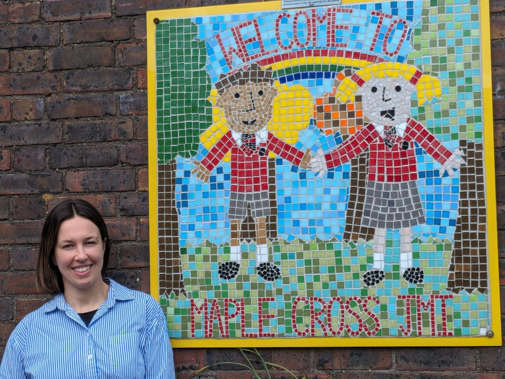 Headteacher Hannah Trickett standing in front of a mural at Maple Cross JMI and Nursery School.