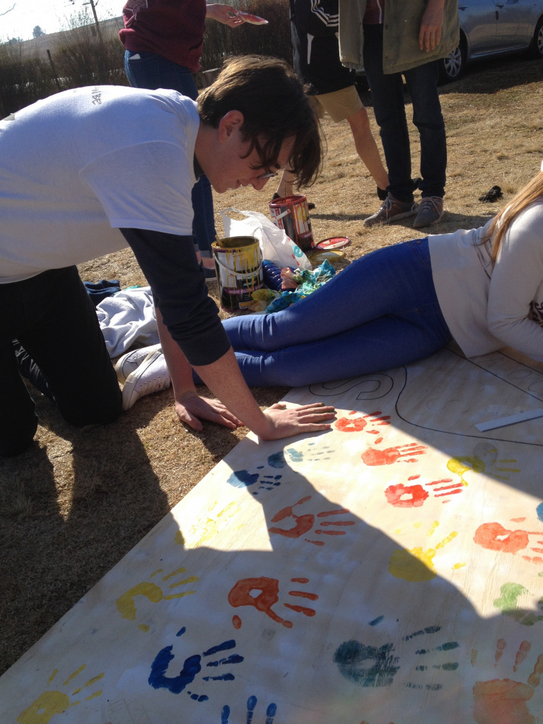 Secondary school boy finger-painting outdoors.