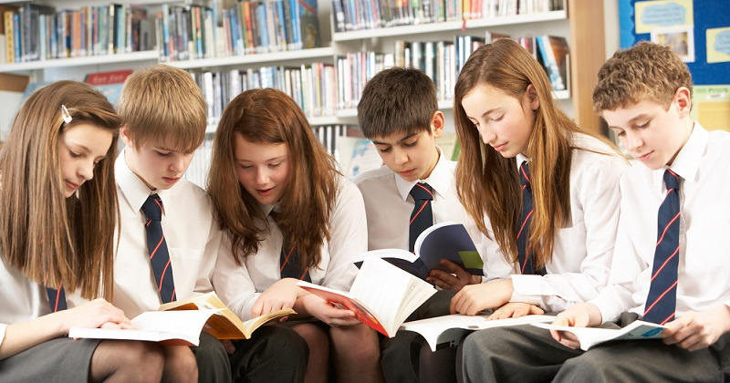 Secondary school boys and girls reading books in a library.