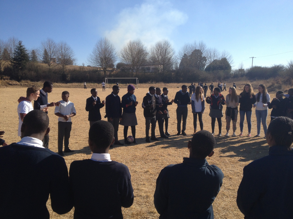 South African and English students standing in a circle on a football pitch.