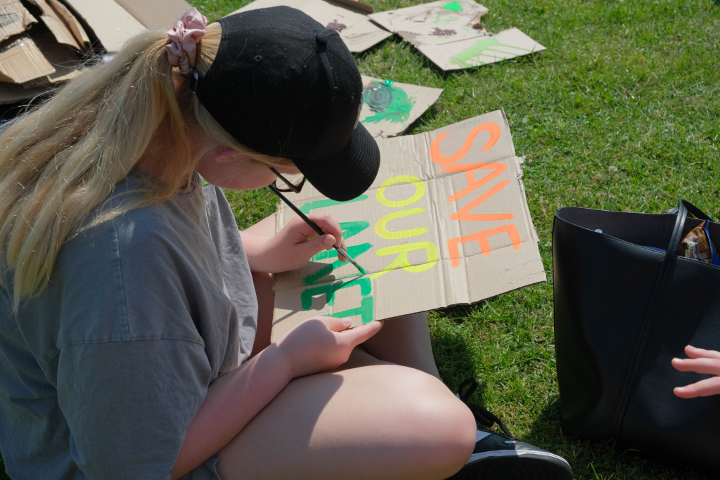 Teenage girl drawing a sign at an environmental rally to protest climate change.