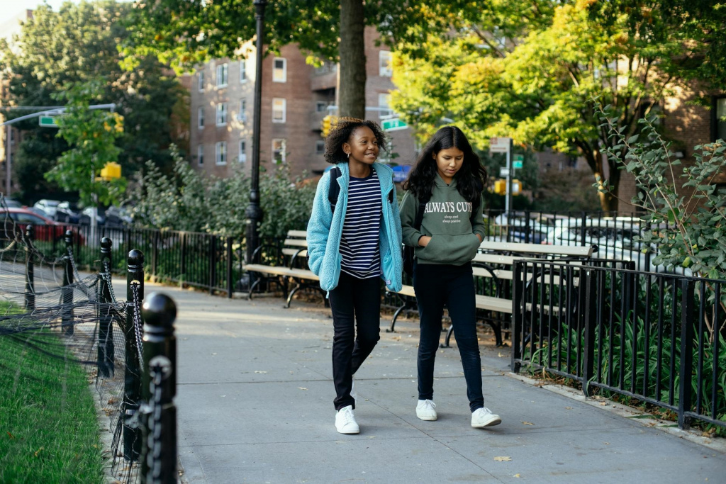 Two teenage girls walking to secondary school through a park.