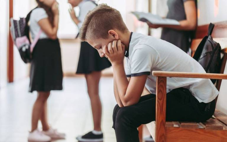 Excluded primary school boy sitting outside classroom.