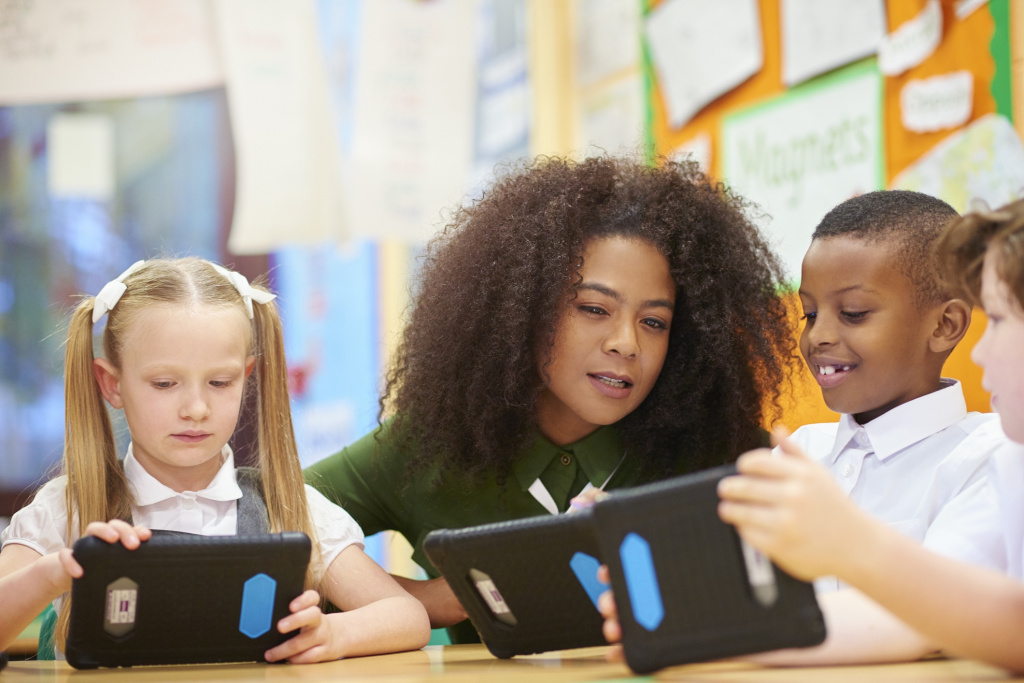 Primary school children and teacher looking at tablets in a classroom.