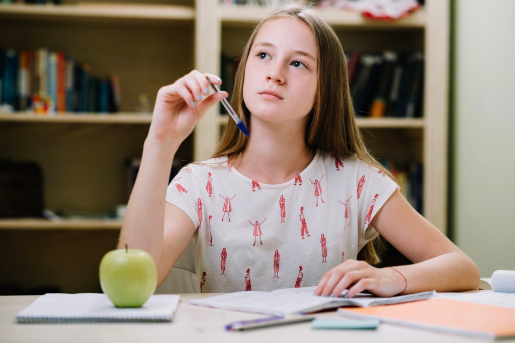 Thoughtful teenage secondary school girl studying with an apple at her desk.