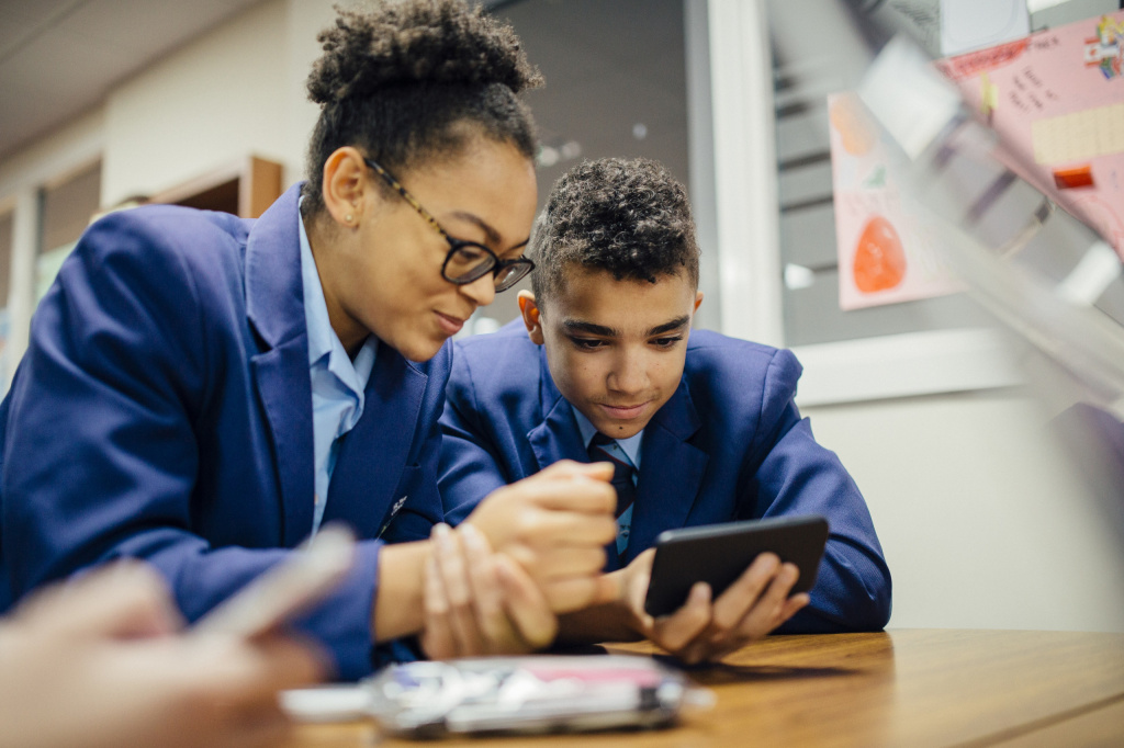 Two secondary school students sitting at a table looking at a smartphone.