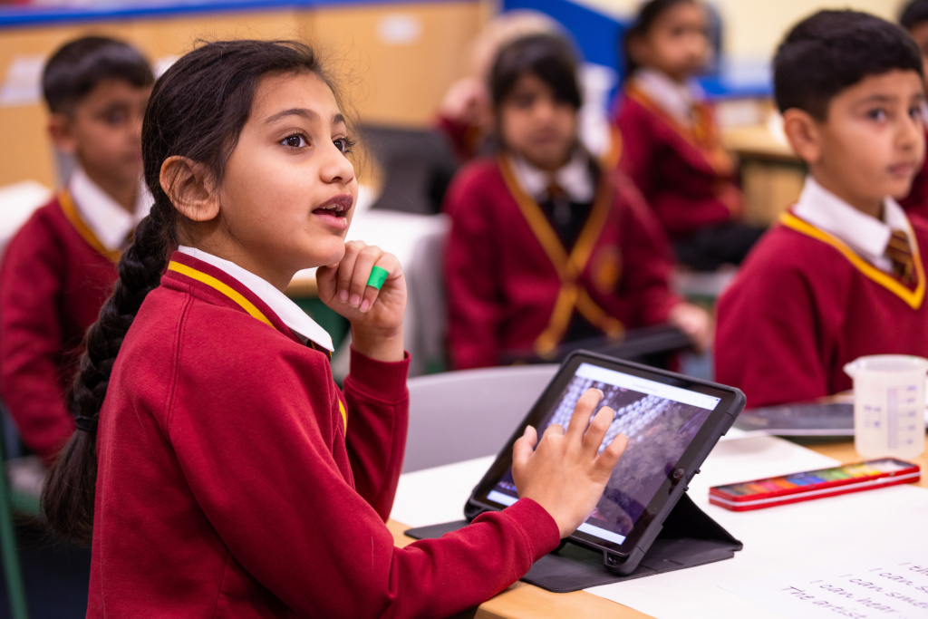 Primary school girl using a tablet in a classroom.