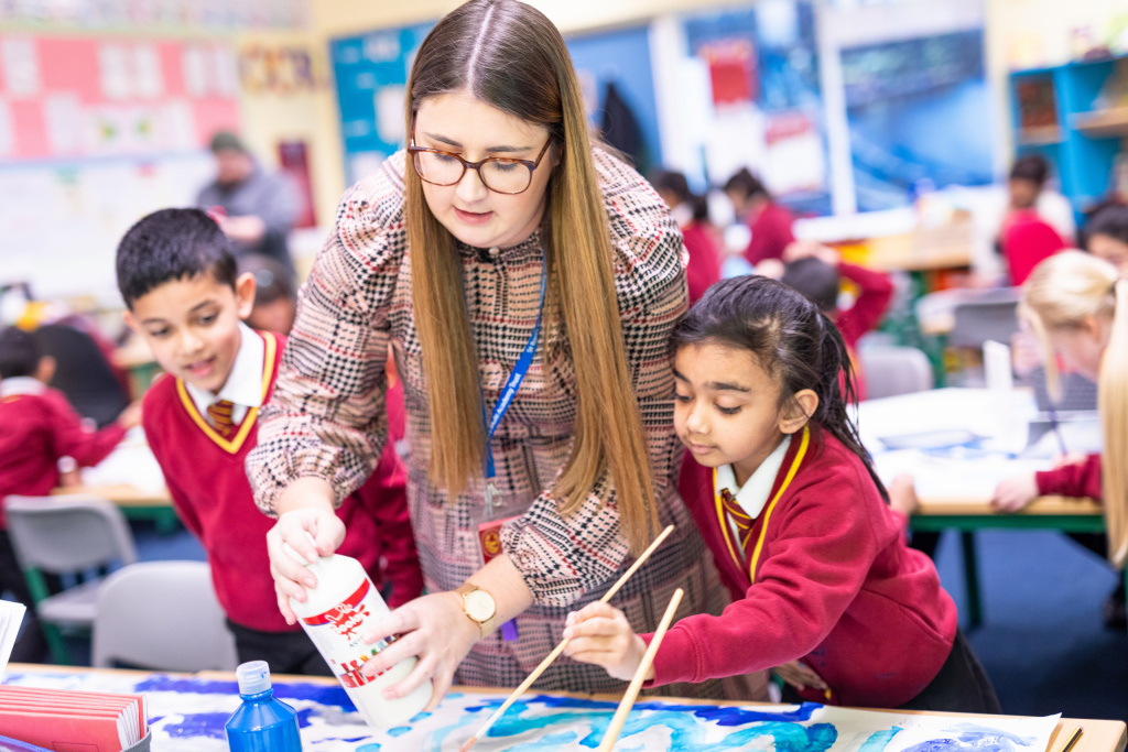 Primary school teacher helping students to paint in an art class.