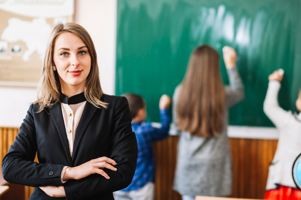 Smiling female secondary school teacher with students writing on a blackboard.