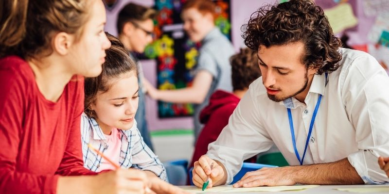 Secondary school teacher working with pupils at a classroom table.