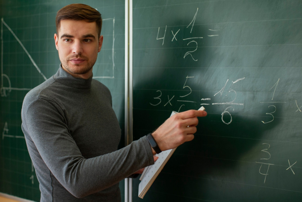 Male maths teacher writing sums on a board in a lesson.