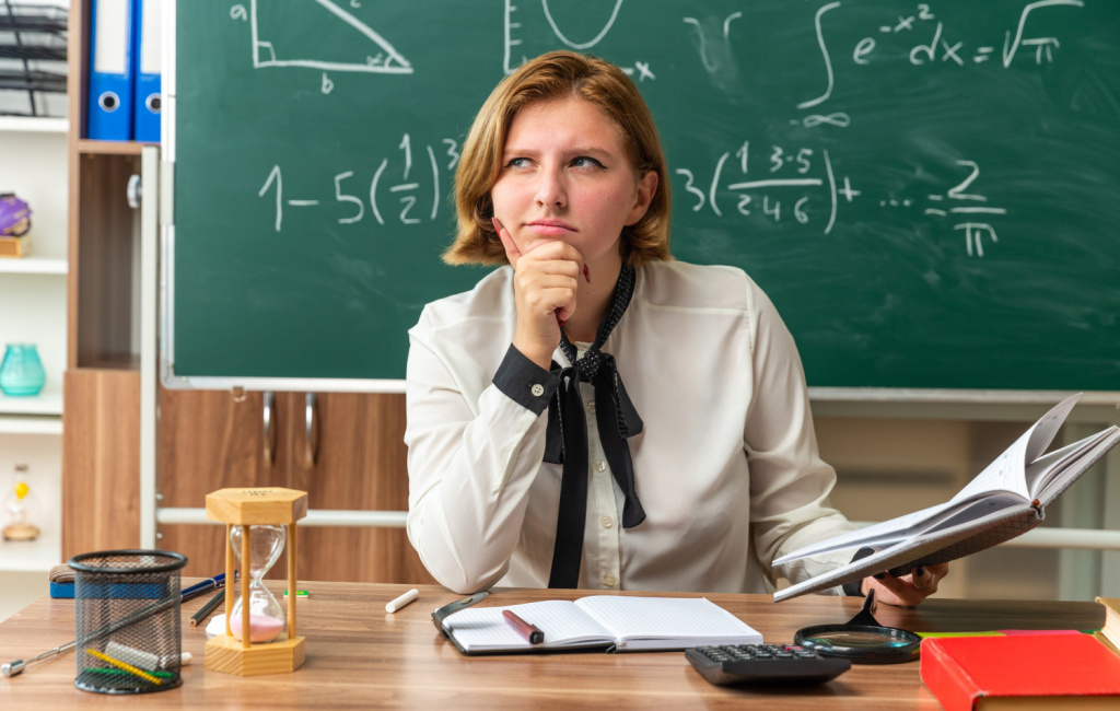 Young female teacher thinking at her classroom desk.