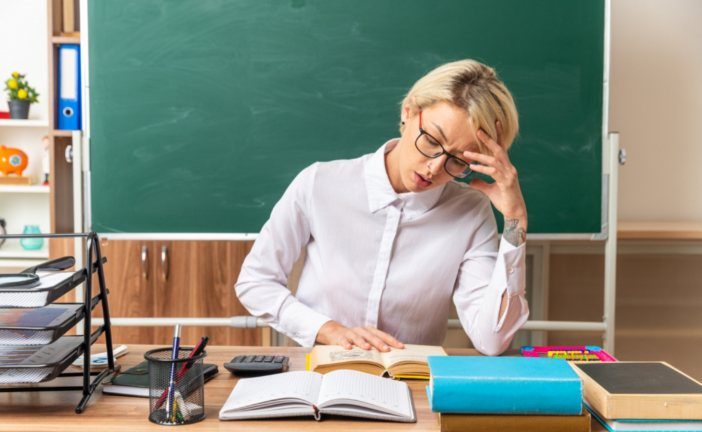 Tired and stressed teacher reading at her desk in a classroom.