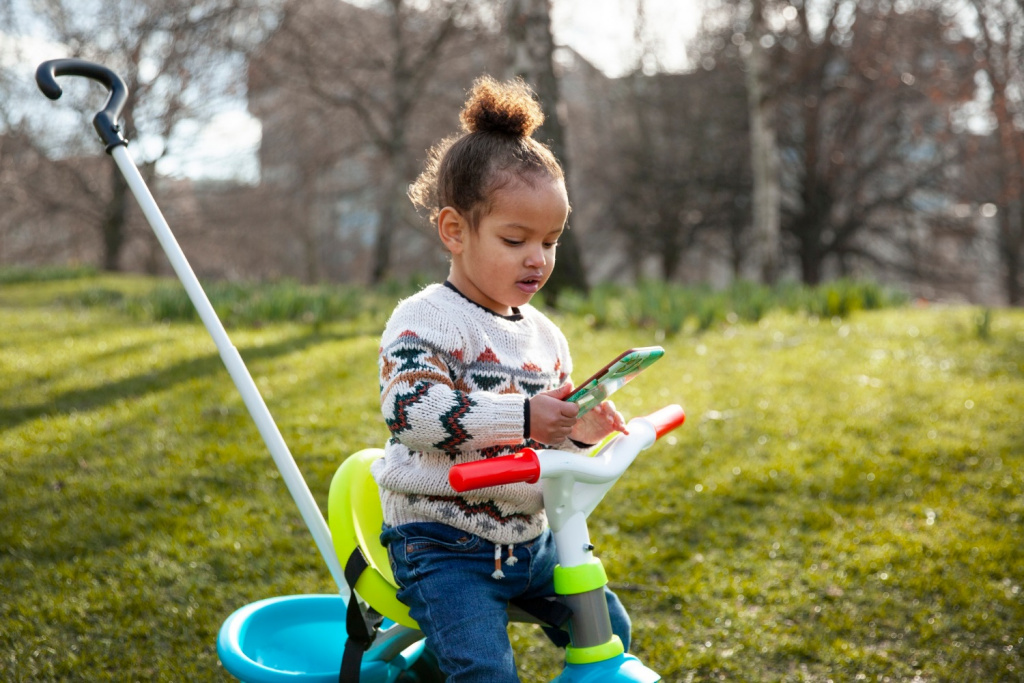 Toddler on a tricycle with a smartphone.