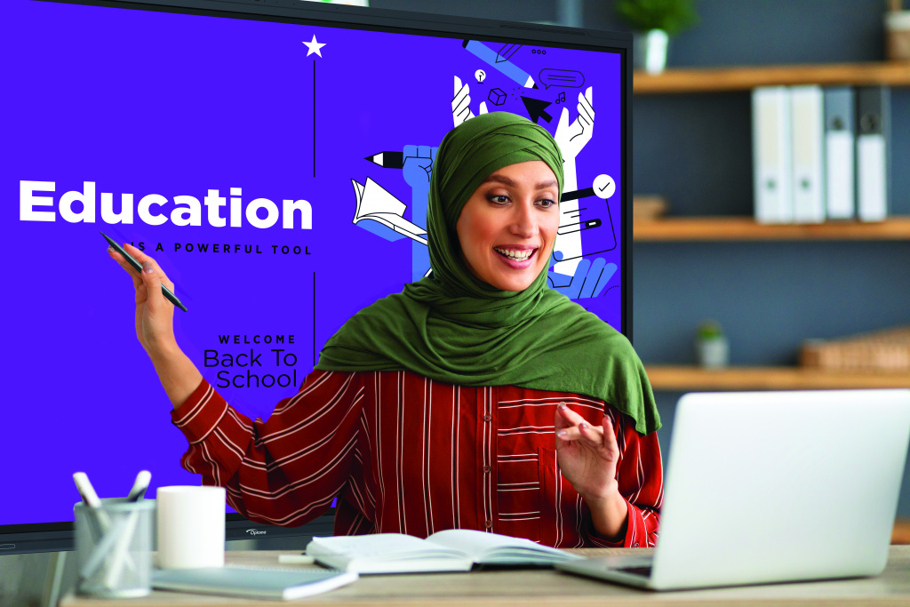 Muslim teacher using an interactive whiteboard as a lesson aid while using a laptop at her desk.